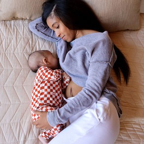 Mom breastfeeding baby on bed. Baby is wearing a Bonsie Footless Checker Bodysuit.