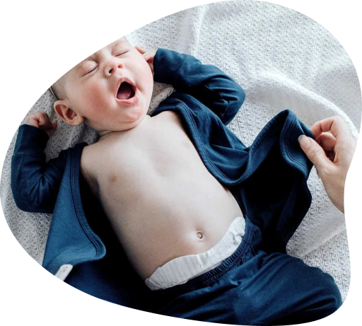 A yawning baby with a bare chest wearing a blue Bonsie romper.