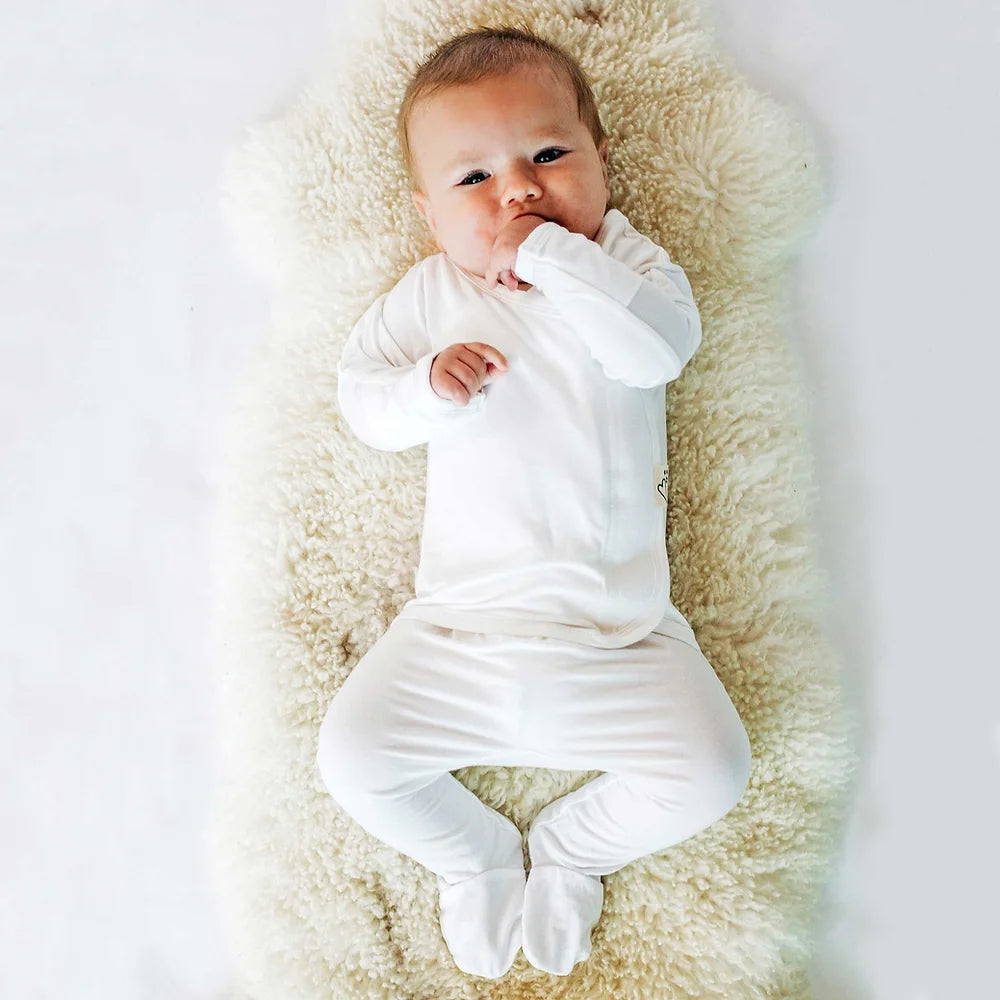 A baby wearing a cozy, long-sleeve white footie lying on a soft blanket.