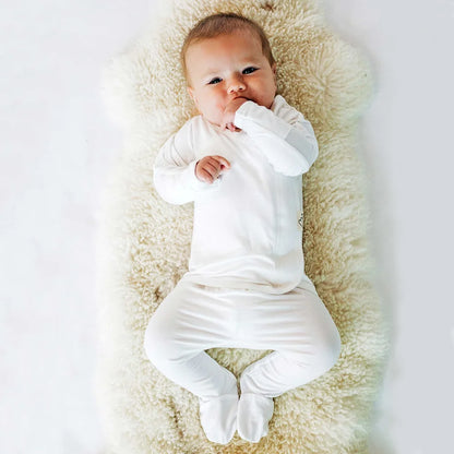 A baby wearing a cozy, long-sleeve white footie lying on a soft blanket.