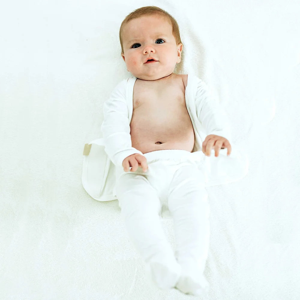 "An infant lying on a white background, dressed in a white onesie with covered feet.
"