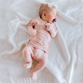 Load image into Gallery viewer, A baby wearing a light peony Bonsie footie lying down on a comfortable mattress.
