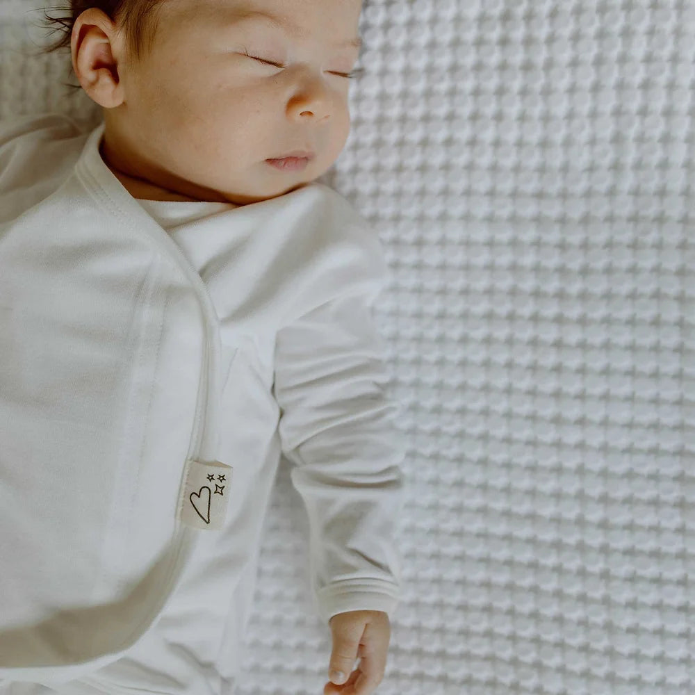 A child lying on a textured mattress wearing a white footie. 